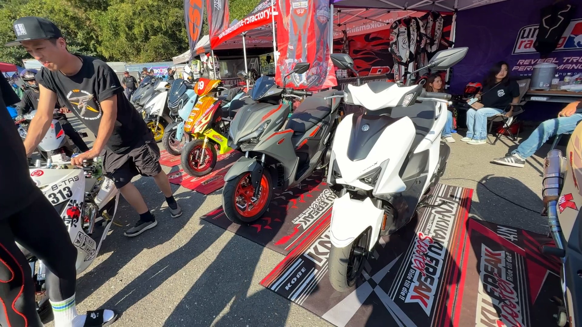 展示マット上に並ぶ白やグレーのスクーターと会場のテント